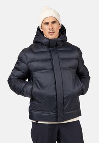 Giacca imbottita blu navy con cappuccio, caratterizzata da una texture liscia e lucida, chiusura con zip e un design trapuntato ben visibile. Calda e isolante.