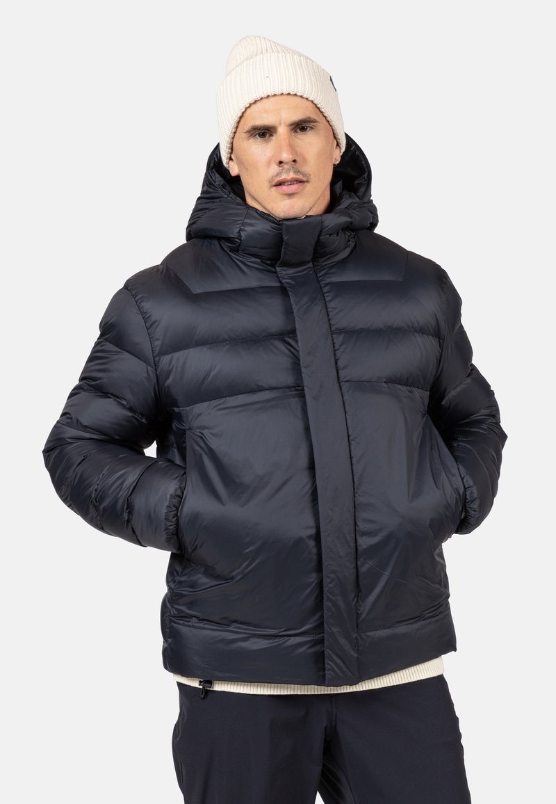Giacca imbottita blu navy con cappuccio, caratterizzata da una texture liscia e lucida, chiusura con zip e un design trapuntato ben visibile. Calda e isolante.