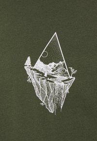 Olivengrünes T-Shirt mit einem weißen grafischen Druck einer dreieckigen Berglandschaft, mit Bäumen und einem Wasserfall, auf einem strukturierten Stoff.