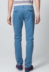 Ljusblå chinos med slim fit, som har två bakfickor med knappstängning och flat front. Slät bomullstyg, minimalistisk design.