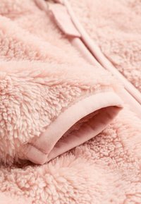 Tissu en polaire rose pâle avec une texture douce et pelucheuse. Doté d'un poignet lisse et élastique et d'une finition de couture nette.