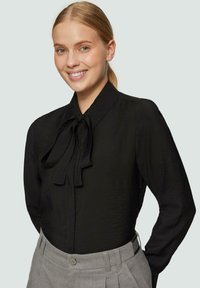 Schwarze Bluse mit hohem Kragen und Bindedetail, aus leichtem Stoff; hat lange Ärmel und eine strukturierte Oberfläche.