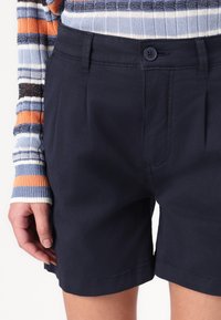 Marinblå bomullsshorts med framfåll, en enstaka knappstängning och en slät yta, kombinerat med en flerfärgad randig stickad topp.