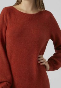 Pull en tricot couleur rouille avec un large col, des manches longues et une finition douce et texturée. Présente une coupe décontractée et des détails côtelés.