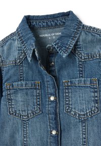 Jeanshemd met een button-down kraag, twee borstzakken en parelknopen. Heeft een vervaagde blauwe wassing en zichtbare stikdetails.