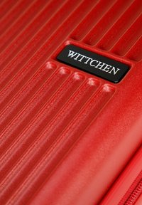 Červený tvrdý kufr s žebrovaným povrchem. Obsahuje černou logo desku se slovem "WITTCHEN" a hladký zip. Kompaktní, odolný design.