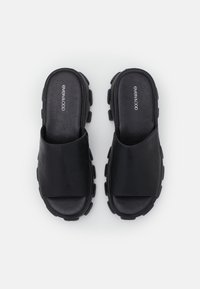 Chanclas de slide negras hechas de cuero suave, con una correa ancha, plantilla acolchada y suela de goma gruesa con detalles de tracción.