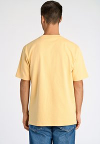 T-shirt giallo chiaro a maniche corte realizzato in cotone, con colletto girocollo classico e vestibilità rilassata. Cuciture visibili lungo le cuciture.