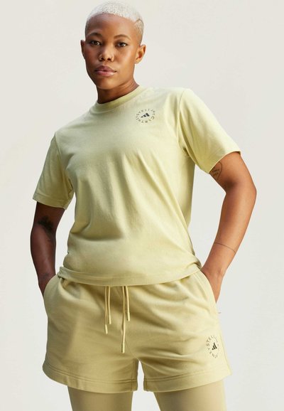 Ensemble t-shirt et short en coton jaune clair avec une coupe décontractée. Présente un logo circulaire, une taille à cordon de serrage, une texture lisse et des manches courtes.