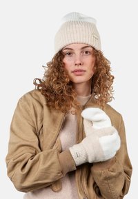 Beige knit beanie with white stripes, paired with beige and white gloves featuring a ribbed cuff. Model wearing a tan bomber jacket.