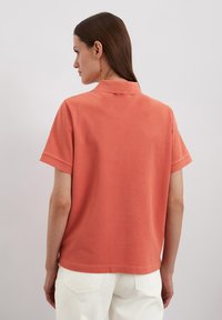 Korte mouwen polo shirt in koraalkleur, gemaakt van zachte katoen. Heeft een klassieke kraag, een effen ontwerp en een rechte zoom.