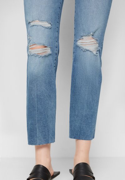 Lençóis de ganga azul claro, com joelhos rasgados, apresentando um corte straight-leg e bainha desfiada. Combinados com sandálias pretas de dedos à mostra.
