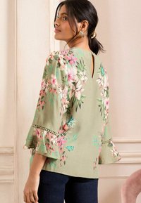 Floral blouse in light green fabric with bell sleeves, featuring pink and blue floral prints and a back keyhole detail.