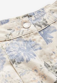 Blommigt denimtyg med beige bas, prytt med blå, gröna och mjukt orange blommor samt en metallknapp vid midjan.