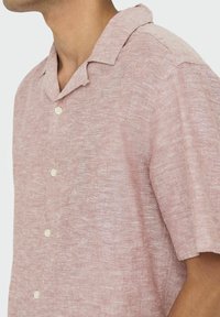 Camisa de manga corta de color rosa claro, confeccionada con tela texturizada, que presenta un cuello tipo rever y botones blancos a lo largo del frente.