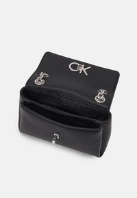 Zwarte leren handtas met een zilveren CK-logo, voorzien van twee metalen sluitingen en een gestructureerde afwerking. Het interieur heeft meerdere vakken.