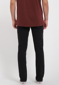 Black denim jeans with a slim fit and classic five-pocket design, paired with a maroon t-shirt. Visible stitching and simple hardware accents.
