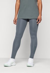 Pilki sportiniai legginsai su prigludusia forma, kuriuose kairiajame kelnyje yra subtilus tamsiai žalias logotipas "BORG". Lygi, tampri medžiaga.