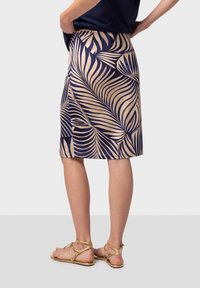 Falda lápiz azul marino con un patrón de hojas de palma en un tono beige claro, de textura suave, hasta la rodilla, combinada con sandalias doradas.