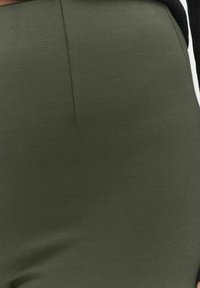 Yksiväriset, oliivinvihreät korkeavyötäröiset housut, jotka on valmistettu pehmeästä ja joustavasta kankaasta. Sisältää etusauman yksityiskohdan ja joustavan vyötärön mukavuutta varten.