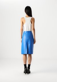 Modrá kožená midi sukně se střihovým střihem, detailním zipem na zadní straně a rozparkem. V kombinaci s bílým ribbed topem a černými botami na podpatku.