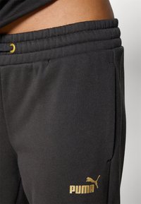 Schwarze Sweatpants aus weichem Material mit einem Kordelzugbund, Seitentaschen und einem goldenen Puma-Logo am linken Bein.