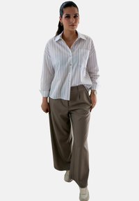Witte button-up shirt met lichte verticale strepen, gecombineerd met losse beige broeken en witte sneakers, met een relaxte pasvorm en een zakdetail.