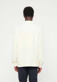 Ανοιχτό κίτρινο, μακρ υμάνικο πουκάμισο με υφή, γιακά, ίσια γραμμή και χαλαρή εφαρμογή. Διαθέτει μανσέτες με κουμπιά και διακριτικό υφαντό σχέδιο.