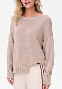 Beżowy sweter dzianinowy z szerokim dekoltem, ściągaczami na rękawach i lekko skróconym dołem. Posiada małą metkę z boku.