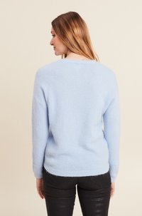Maglione azzurro chiaro caratterizzato da una texture morbida e pelosa, colletto a girocollo e vestibilità rilassata. Maniche lunghe con polsini a costine, abbinato a pantaloni scuri.