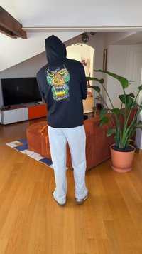 Svart hoodie med en färgstark gorillagrafik på ryggen, kombinerad med ljusgråa sweatpants och bruna skor, i en mysig inomhusmiljö.
