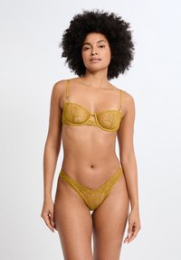 Sujetador amarillo bordado y tanga a juego con un diseño floral, tela transparente y delicado ribete de encaje, destacando detalles intrincados.