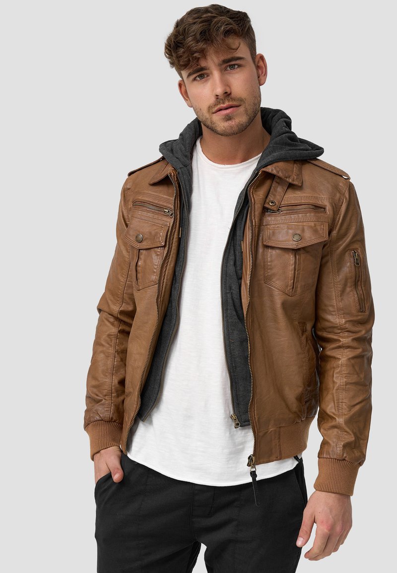 Veste en cuir marron avec une couche intérieure à capuche grise, comportant plusieurs poches zippées et boutonnées, des poignets côtelés et une fermeture éclair.