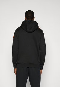 Μαύρο φούτερ με κουκούλα κατασκευασμένο από απαλό ύφασμα, με κορδόνι και ριμπ τελείωμα, με πορτοκαλί λεπτομέρειες στους ώμους. Συνδυάζεται με παντελόνι στο ίδιο χρώμα.