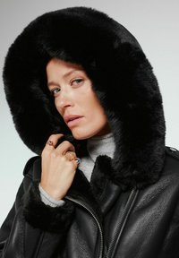 Czarna skórzana kurtka z czarnym, miękkim futrzanym kapturem. Posiada zamek błyskawiczny, miękkie mankiety oraz szary golf pod spodem.