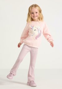 Lyserød fleece sweater med et enhjørning design, parret med lyserøde, flagrende bukser og matchende sneakers. Blød tekstur, afslappet pasform.