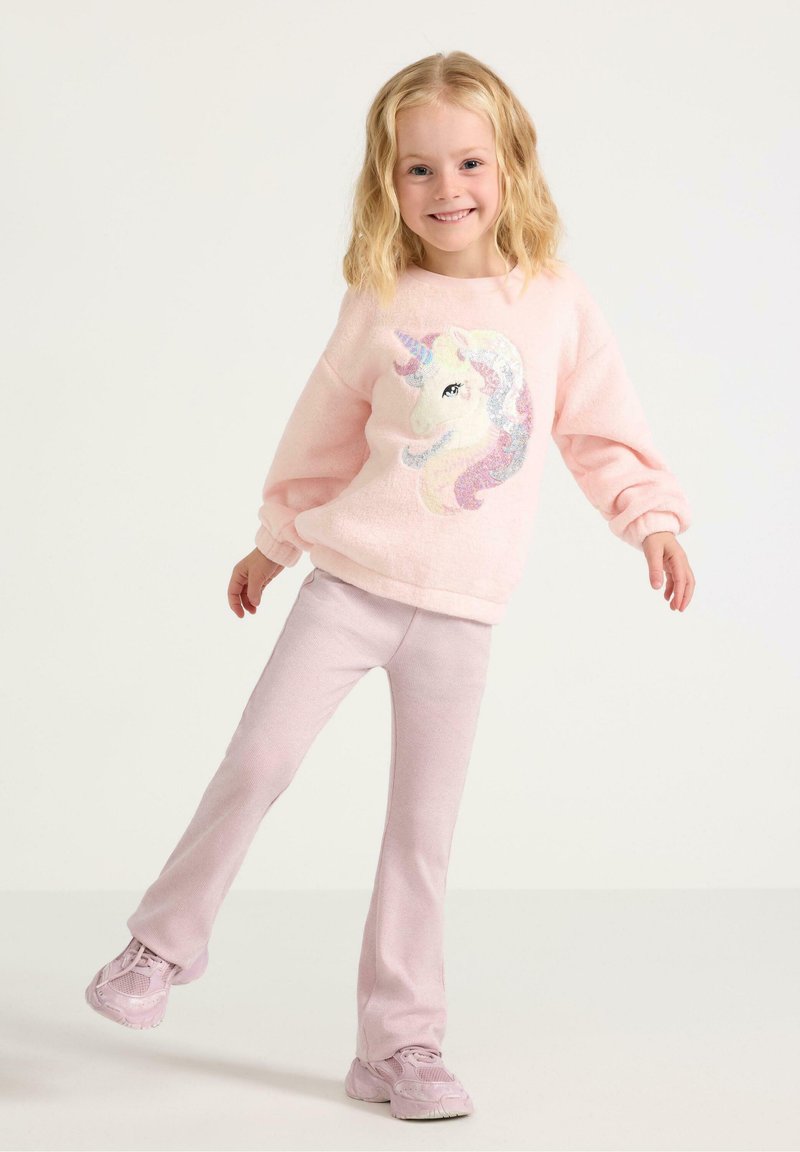 Lyserød fleece sweater med et enhjørning design, parret med lyserøde, flagrende bukser og matchende sneakers. Blød tekstur, afslappet pasform.