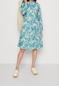 En tealblommig klänning med krage, långa ärmar och samlad midja. Matchad med beige träklackar. Mjuk tygkänsla.