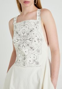 Witte jurk met complexe zilveren borduursels met een bloemen- en geometrisch ontwerp. Vierkante halslijn, brede banden en zijzakken.