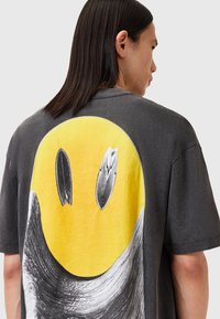 Grå oversized t-shirt med et stort gult smilende ansigt grafisk design med sorte surfboard accenter og svungne sorte detaljer. Korte ærmer.
