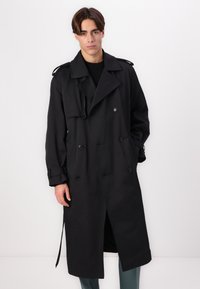 Czarny trenchcoat wykonany z gładkiego materiału, z podwójnym zapięciem, dużym kołnierzem, pagonami na ramionach i bocznymi kieszeniami.