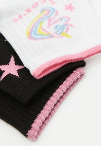 Drei Paar Socken in Schwarz, Weiß und Pink. Die weiße Socke hat ein mehrfarbiges Schwanenmotiv, während die schwarze mit rosa Sternmustern verziert ist.