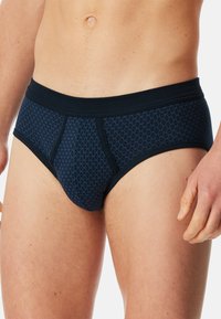 Pánské slipy ve tmavě modré barvě s diamantovým vzorem. Vyrobené z měkké, elastické látky s kontrastním černým pasem.