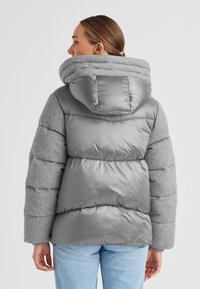 Graue Steppjacke mit einem gesteppten Design und einer gestrickten Kapuze, mit glänzendem Finish, übergroßer Silhouette und gerippten Ärmelakzenten.