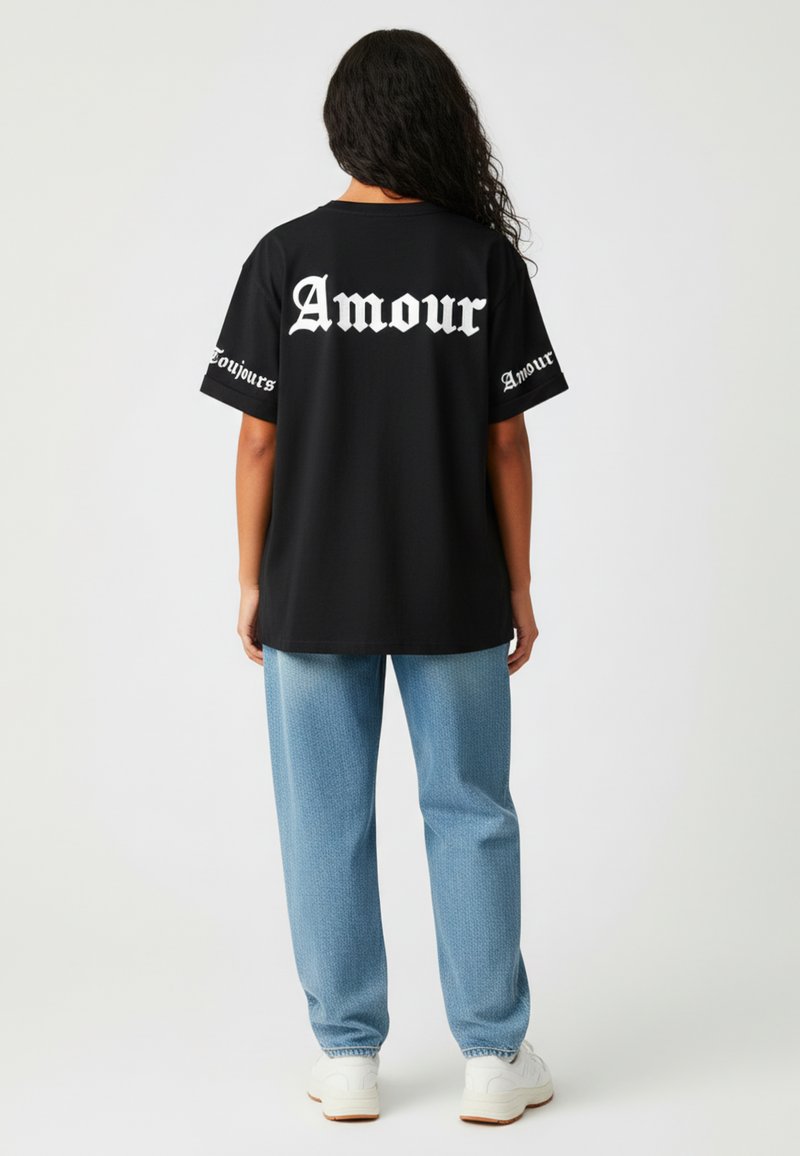 Melna lielizmēra T-kreklu ar baltu gotiskā stila tekstu "Amour" uz muguras un piedurknēm, kombinēts ar gaiši zilām rakstainām biksēm un baltām kedām.