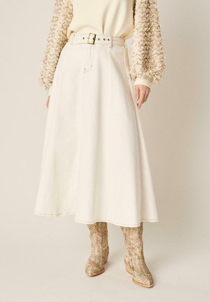 Falda línea A color crema de cintura alta con cinturón, combinada con un top beige de manga larga texturizado y botines hasta el tobillo con estampado de serpiente.