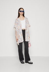 Lahka, vzorčasta kimono v krem barvi z modrim in oranžnim paisley vzorcem. V kombinaciji z belim kratkim topom, črnimi širokimi hlačami in platform čevlji.