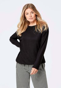 Schwarzes Langarmoberteil mit rundem Ausschnitt, kombiniert mit Hosen im Hahnentrittmuster in Schwarz und Weiß. Weicher Stoff und lockere Passform.