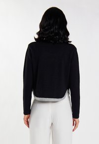 Zwarte cropped trui met lange mouwen, voorzien van een grijze zoom. Zachte textuur met een eenvoudig, strak ontwerp, gezien vanaf de achterkant.