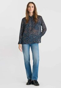 Sheer blue blouse with an abstract pattern, two chest pockets, button-down collar, paired with light blue jeans and black shoes.